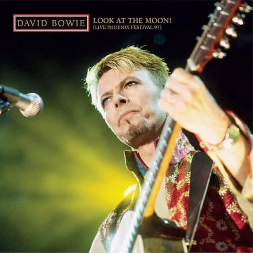 David Bowie performing live on stage playing an acoustic guitar with a microphone nearby.