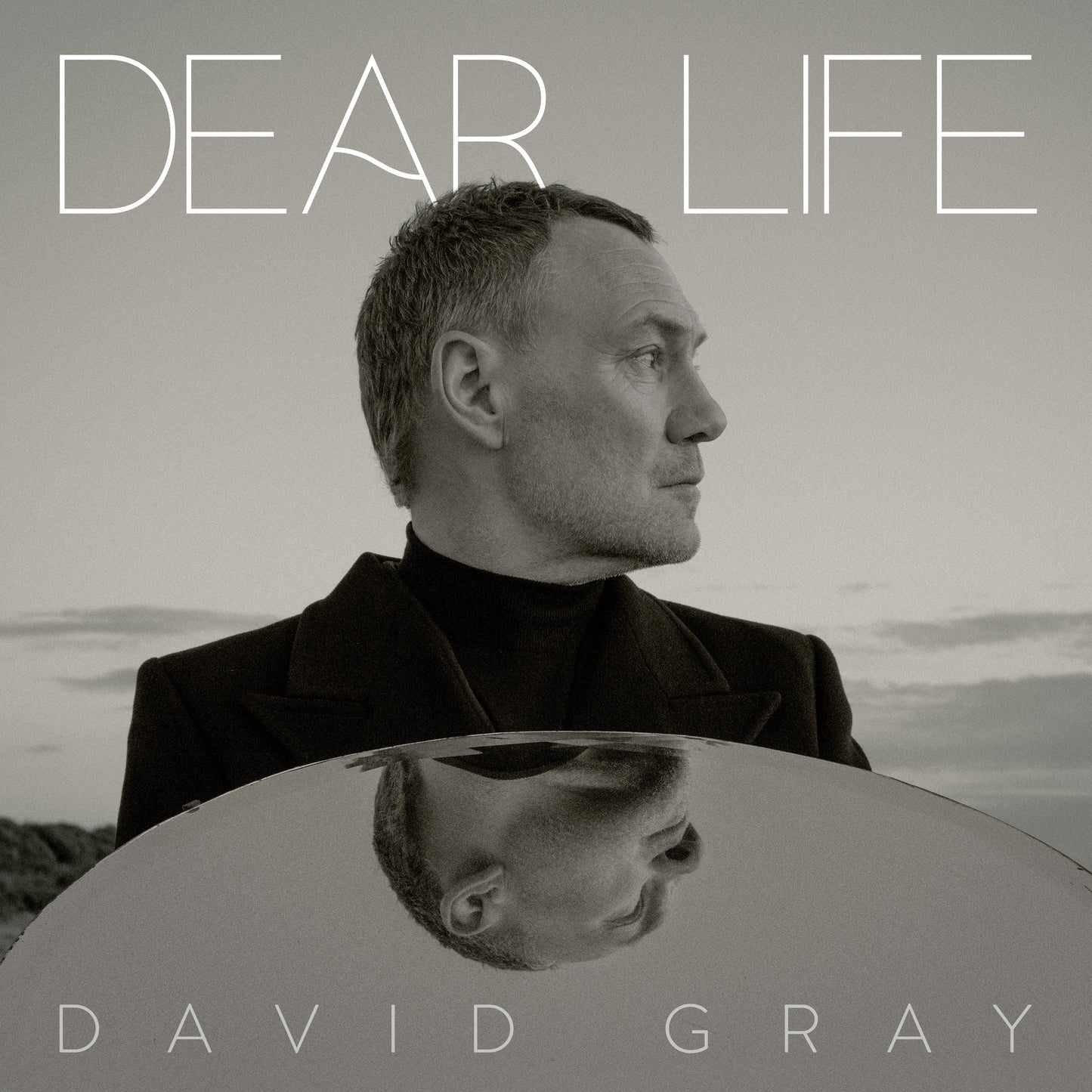 Black and white portrait of David Gray holding a circular mirror reflecting his face.