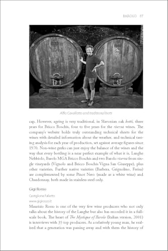 A man stands between two large wooden wine barrels in a cellar.