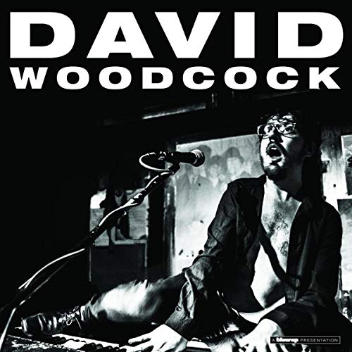 Black and white album cover featuring musician David Woodcock at a keyboard.