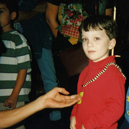A young boy in a red shirt with a snake draped over his shoulder.