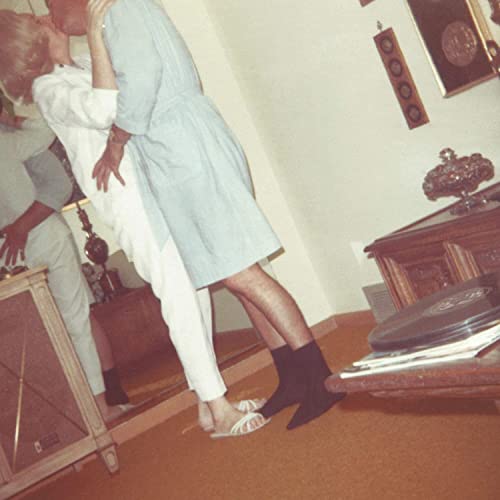 A couple in robes kisses in a room with vintage furniture and carpet.