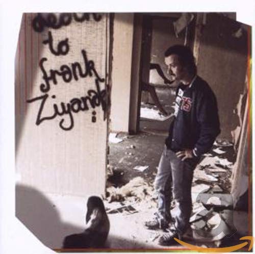 Man stands near graffiti reading “Death to Frank Ziyanak” in a damaged room.