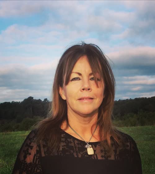 Portrait of a woman with brown hair, outdoors against a cloudy sky.