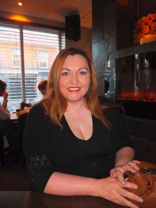 Woman with red hair smiling at the camera in a cafe setting.