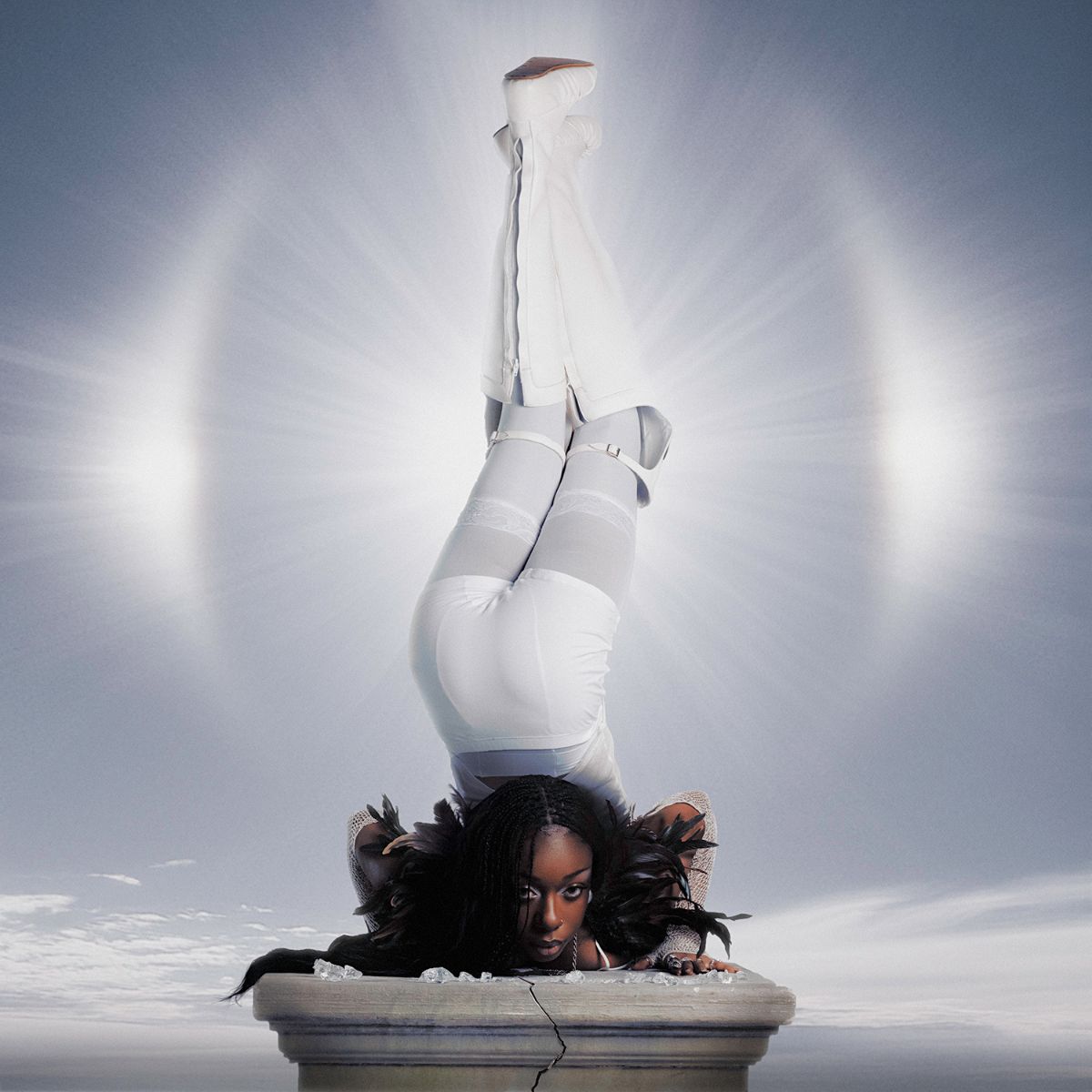 Person in white clothing balanced headstand on a cracked pedestal.
