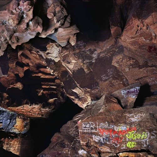 Interior of a dark cave with rocky walls featuring graffiti and deep shadows.