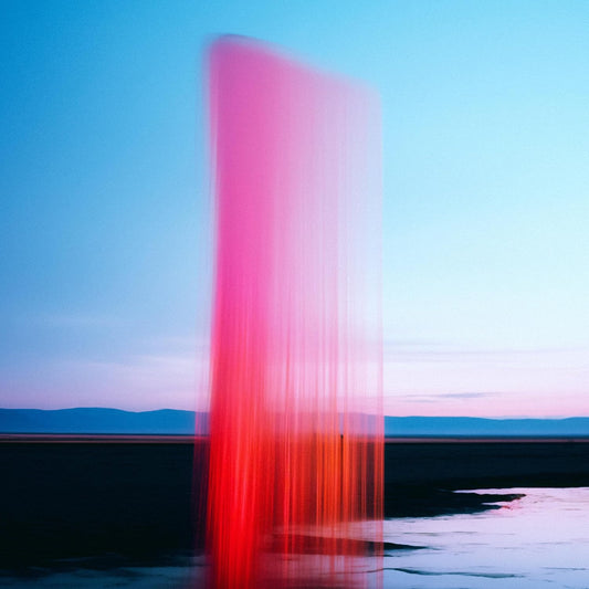 Abstract red vertical light streak over water and distant land.