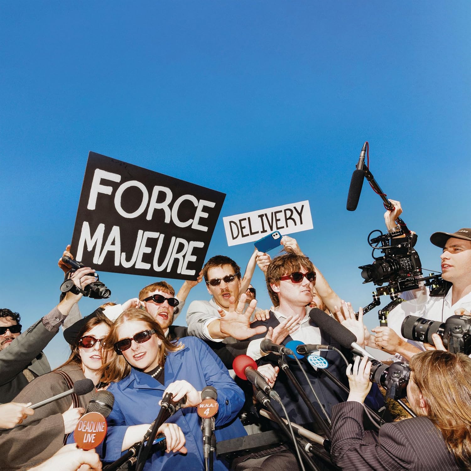 Group holds signs reading “Force Majeure Delivery” surrounded by cameras.