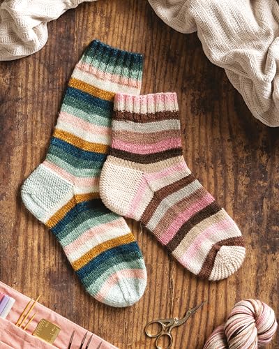 Two hand-knitted striped socks on a wooden surface with knitting tools and yarn.