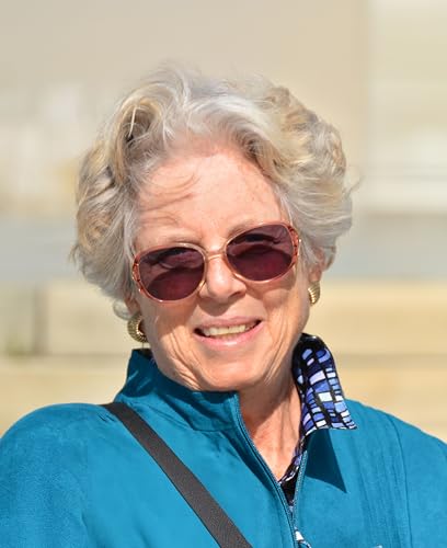 Older woman with short curly hair and sunglasses smiling at the camera.