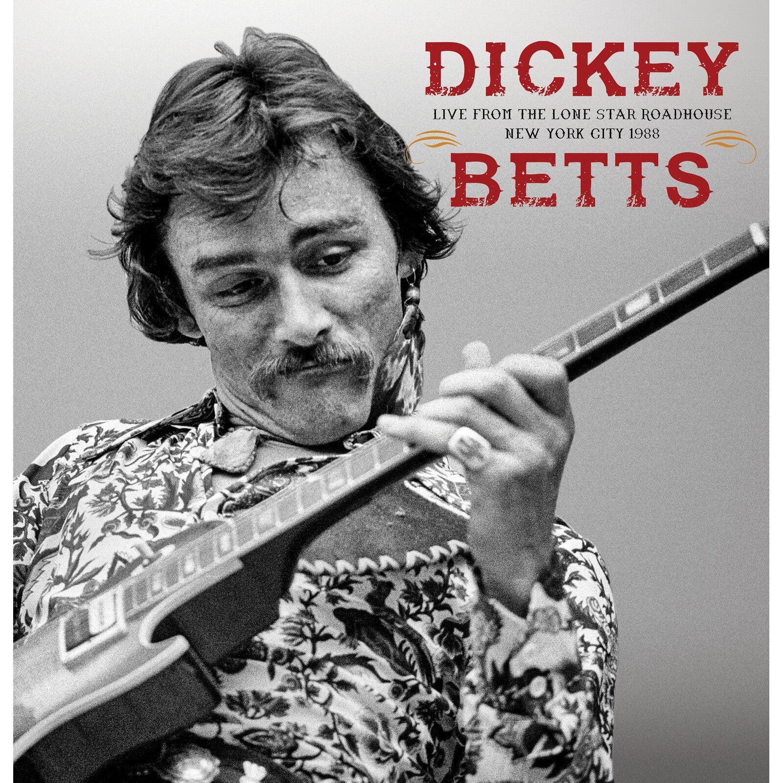 Black and white portrait of Dickey Betts playing a guitar.