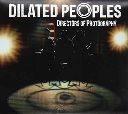 Silhouetted figures of three men stand in a studio lit by two bright spotlights.