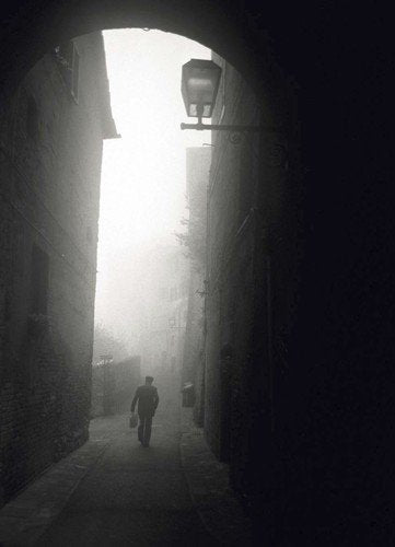 The image shows a black-and-white photograph of a man walking down a narrow, foggy alleyway. For accessibility purposes, a suitable alt text could be: "DVD cover with a man walking down a foggy alleyway."