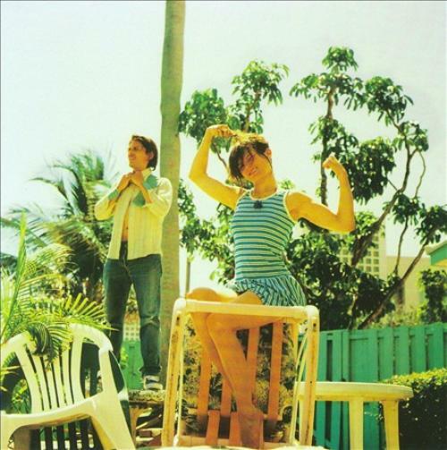 Two people pose outdoors amongst tropical plants and a turquoise fence.