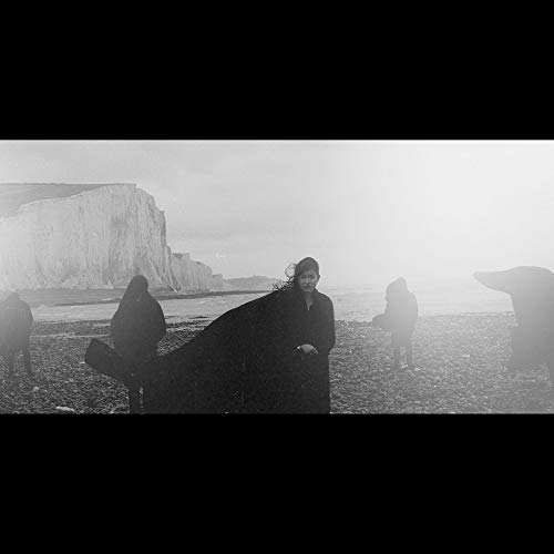 Black and white image of figures in cloaks on a pebble beach.