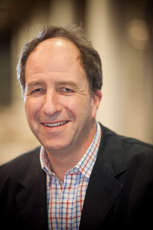 A smiling middle-aged man wearing a plaid shirt and a dark jacket.