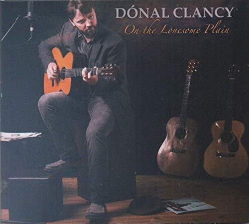 Donal Clancy seated playing guitar, with two other guitars nearby.