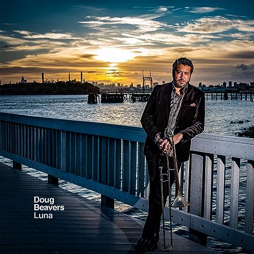 Doug Beavers with trombone, standing on a pier at sunset.