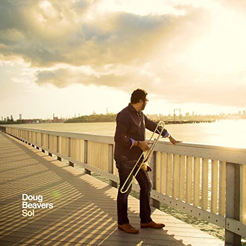 Man with trombone on a bridge overlooking water under a cloudy sky.