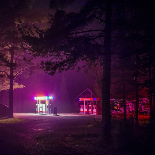 "CD case with neon-lit gas station scene on the cover, surrounded by trees."