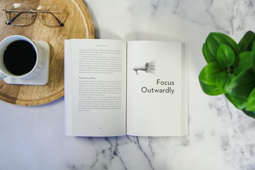 Open book, coffee cup, glasses, and plant on a marble surface.