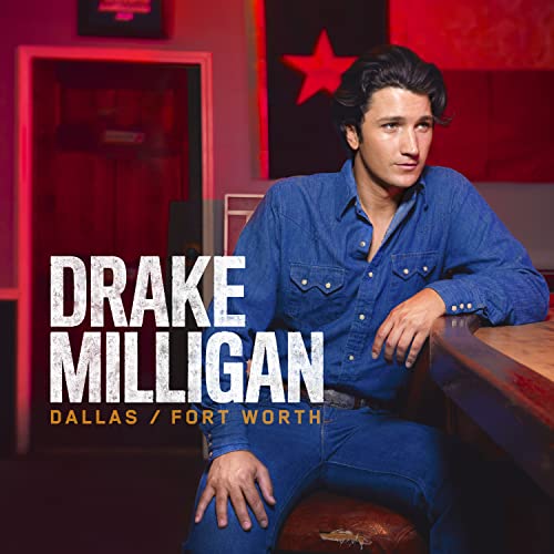 Drake Milligan in a denim shirt sits at a bar with red lighting behind him.