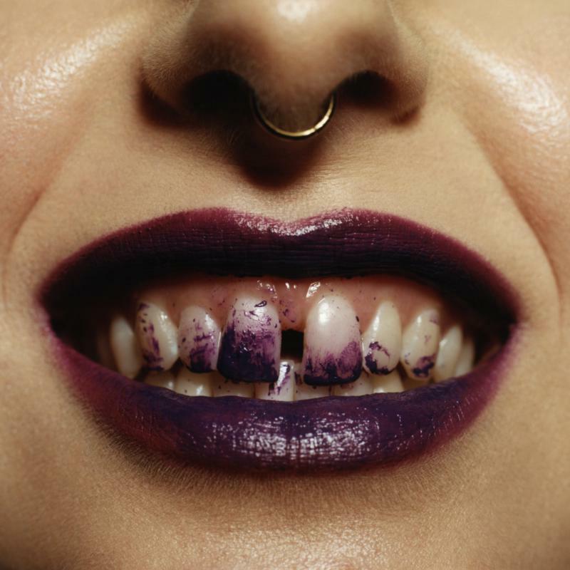 Close-up of lips with dark purple lipstick and painted teeth.