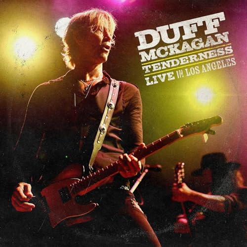 Duff McKagan playing guitar on stage under bright concert lights.