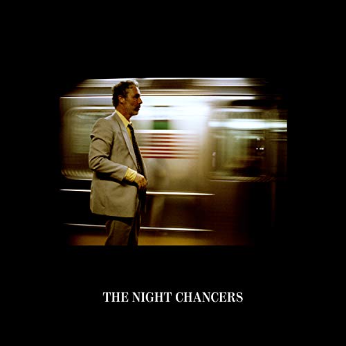 The image is an album cover featuring a man in a suit. The alt text: "A man in a suit walks past a blurred train."