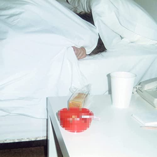 A person hiding under white bedsheets with a cup and red bowl on table.