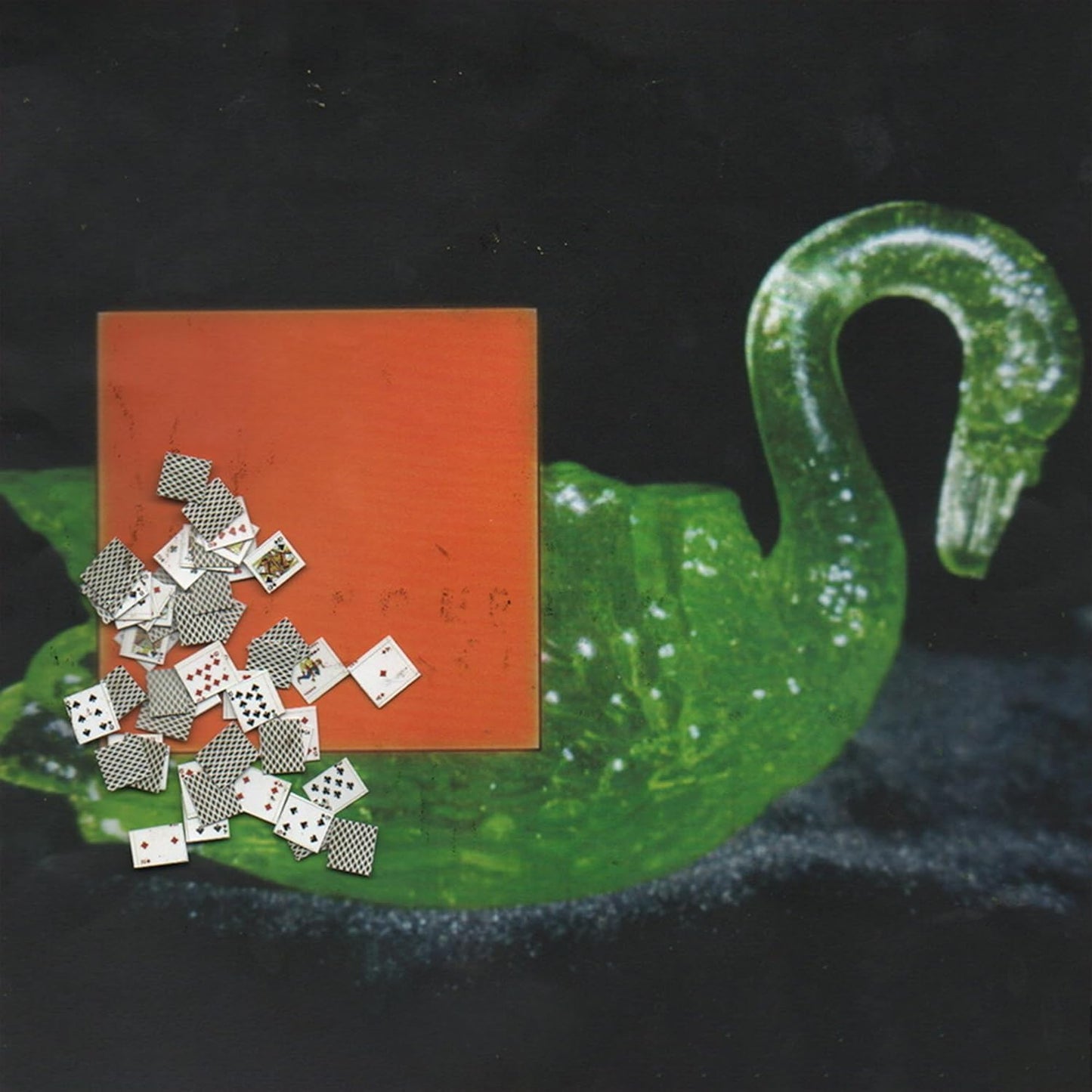 A green glass swan sculpture with a square orange card and scattered playing cards.