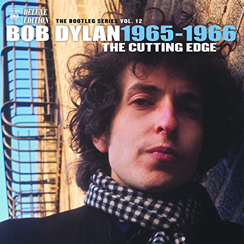 Close-up portrait of Bob Dylan wearing a checkered scarf against a brick wall.