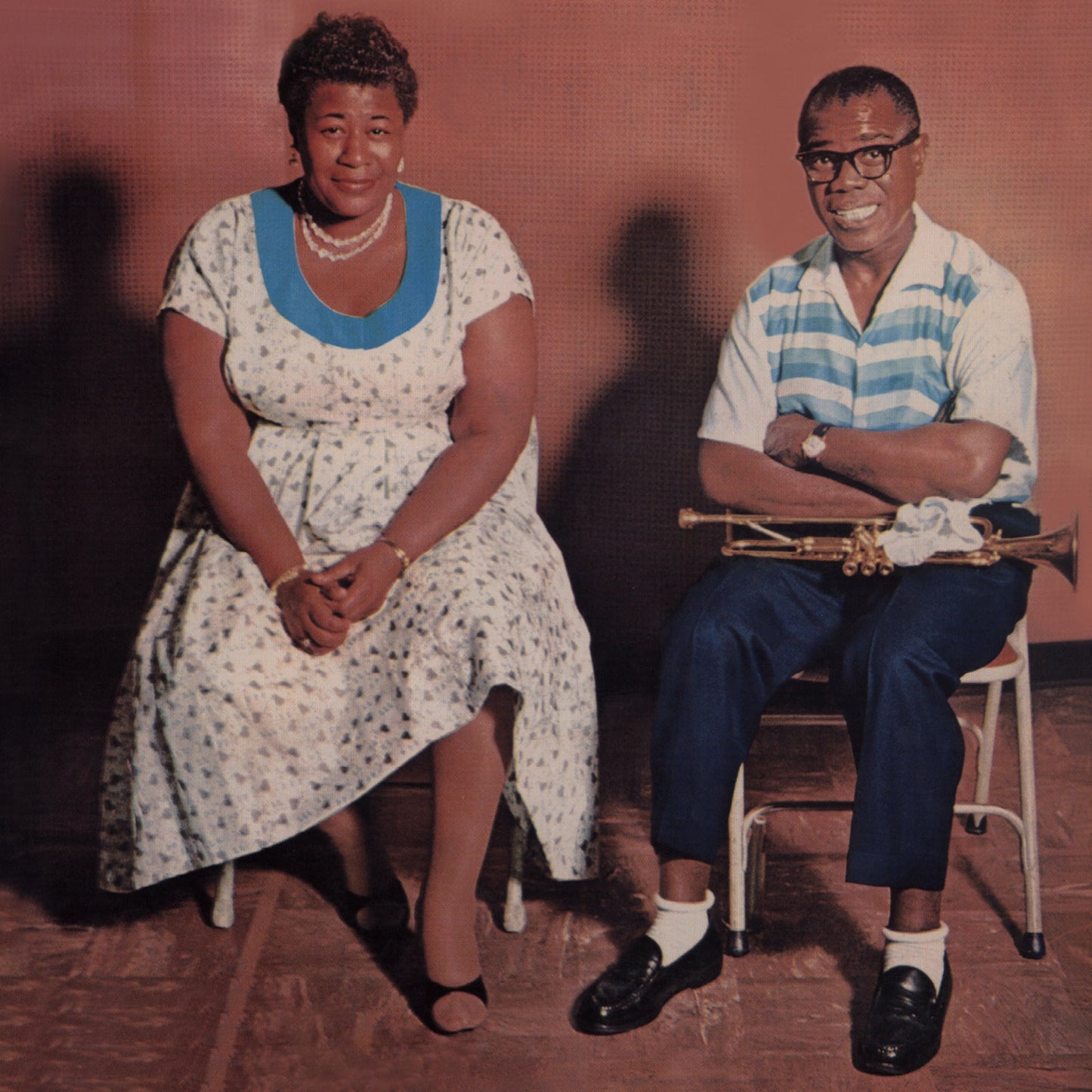 Ella Fitzgerald and Louis Armstrong seated, smiling, with a trumpet.