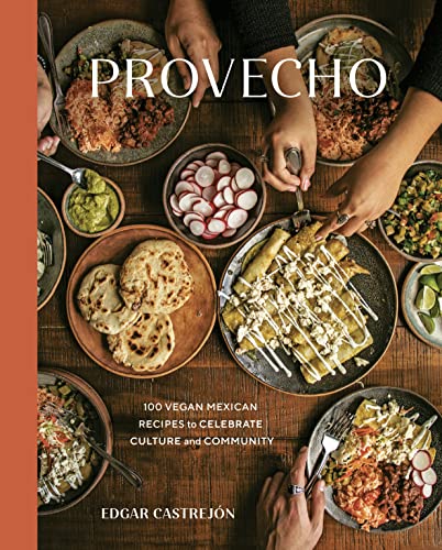 Overhead view of a wooden table filled with various Mexican dishes and hands eating.