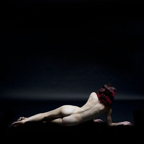 Nude figure with red hair lying prone against a dark background.