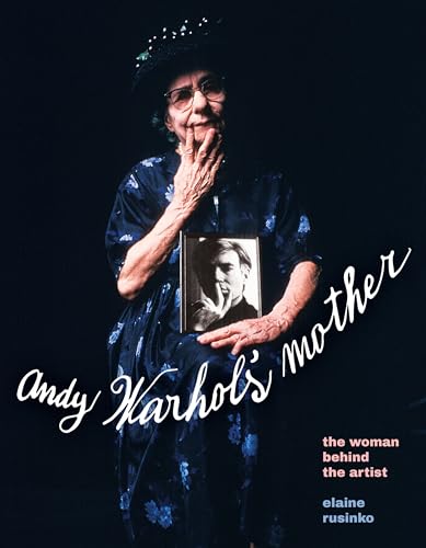 Older woman in floral robe holding a framed photo of Andy Warhol.