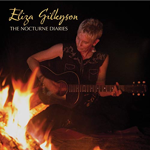 Eliza Gilkyson playing an acoustic guitar by a campfire at night.