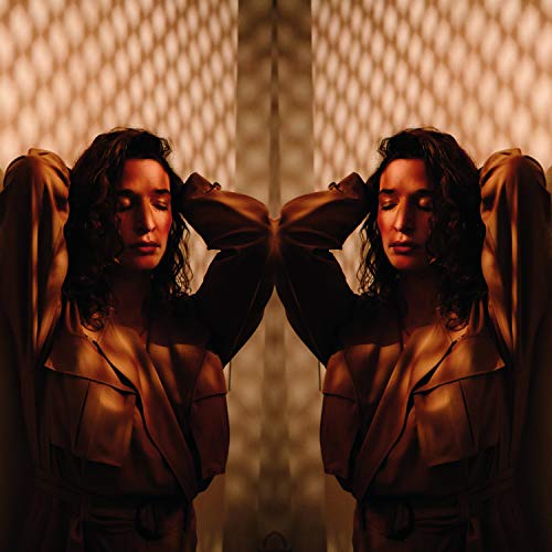Symmetrical portrait of a woman with curly hair, arms raised, bathed in light.