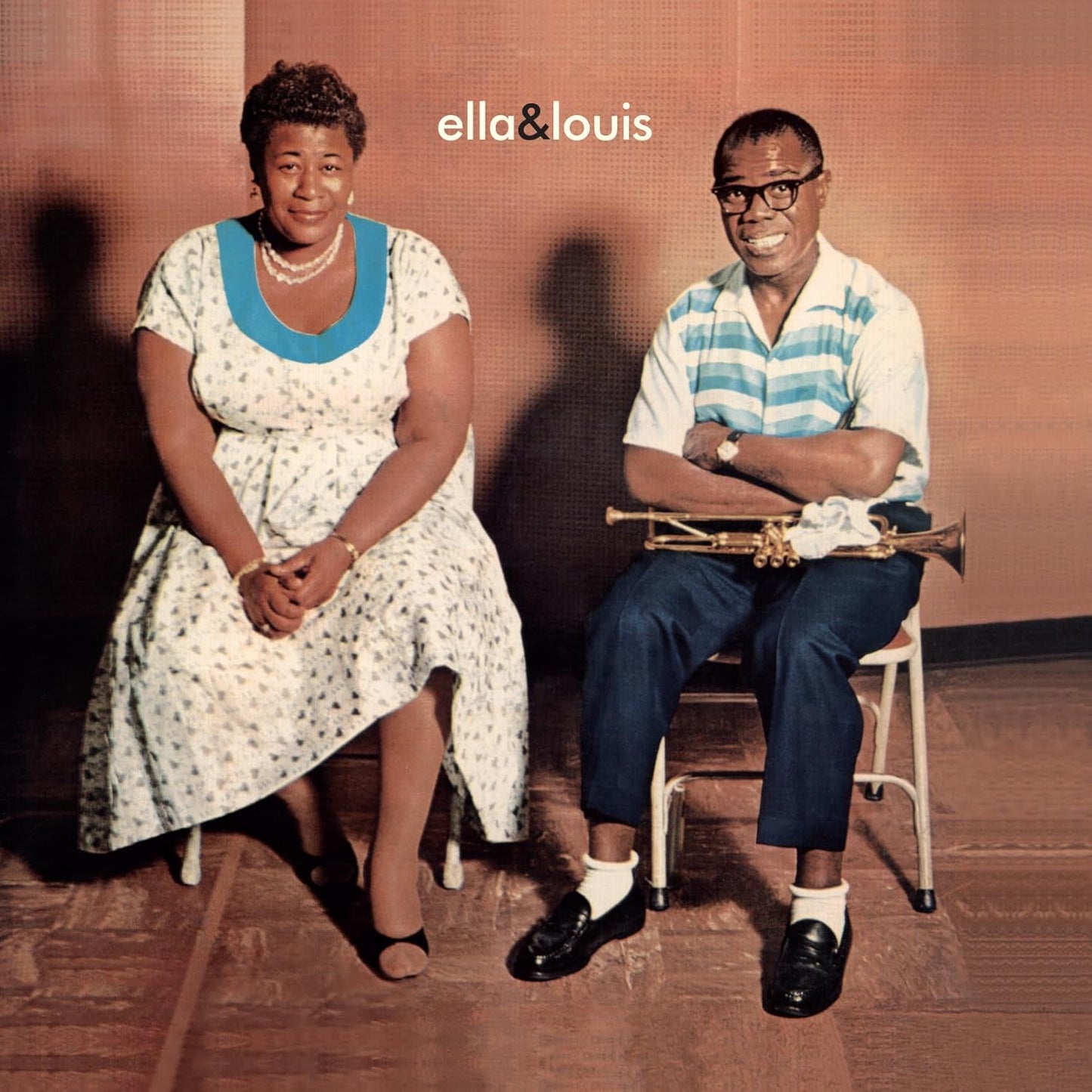 Ella Fitzgerald and Louis Armstrong sitting on chairs with a trumpet in a studio.
