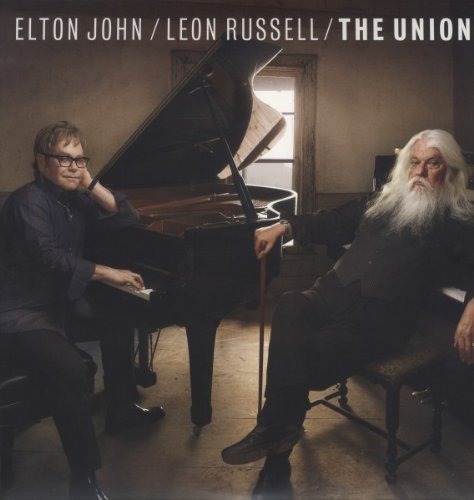 Elton John and Leon Russell seated with a grand piano.