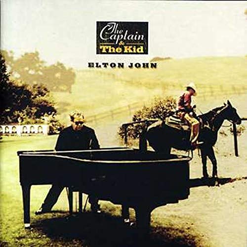 Elton John sitting at piano outdoors with a child on a horse beside him.