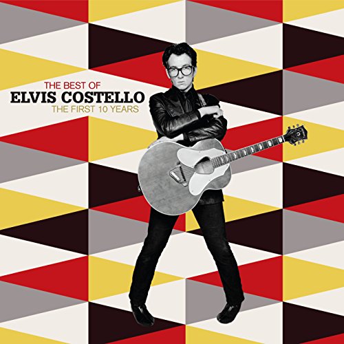 Elvis Costello wearing glasses and a leather jacket, holding an acoustic guitar against geometric background.