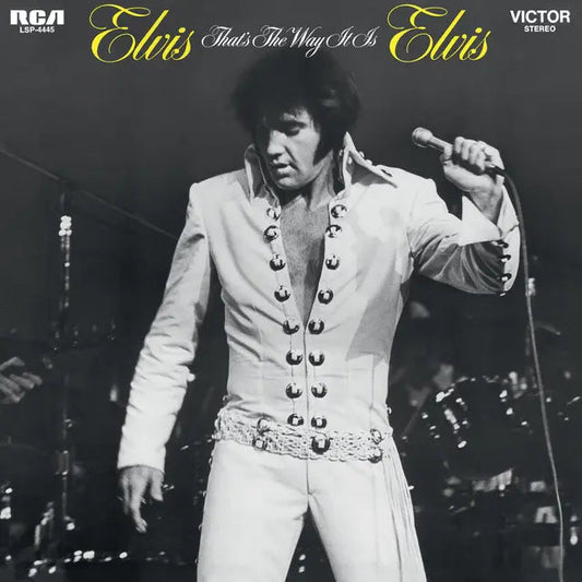 Black and white photo of Elvis Presley performing on stage in a white jumpsuit.