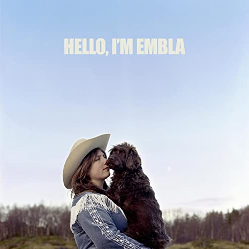 Woman in a hat nuzzles a large, dark dog against a blue sky.