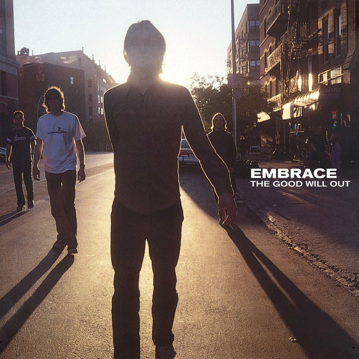 Silhouetted figures walking down a sunlit city street, album cover.