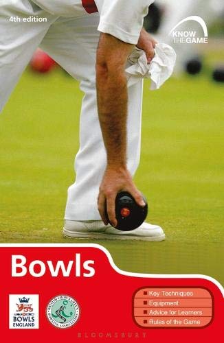 Man in white clothing holding a black bowling ball on a green field.