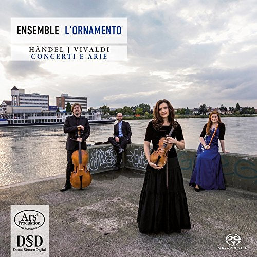 Classical musicians with instruments pose by a riverfront with buildings.