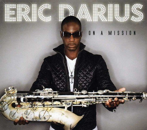 Man holding saxophone, wearing black jacket and sunglasses, against a gray background.