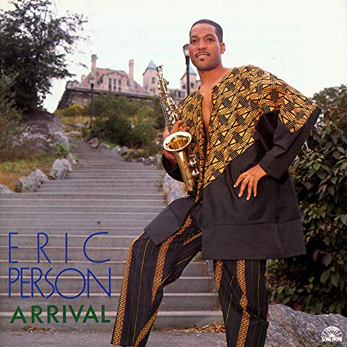 Saxophonist Eric Person in patterned clothing stands before a large building.
